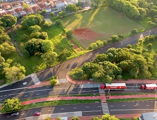 Vista aérea de camiones de Coca-Cola circulando por una ruta rodeada de vegetación y ciclovías, simbolizando el equilibrio entre la logística y el cuidado del medio ambiente.